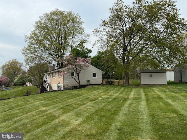 view of yard featuring fence, a storage unit, and an outbuilding