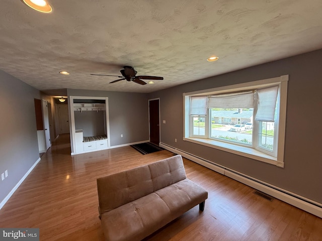 living area with a ceiling fan, baseboards, baseboard heating, and wood finished floors