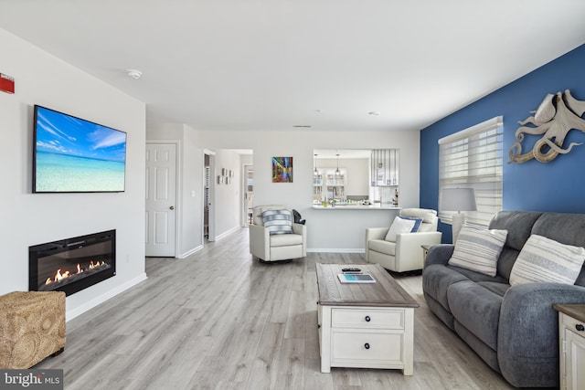 living room featuring a notable chandelier, a glass covered fireplace, light wood-style flooring, and baseboards