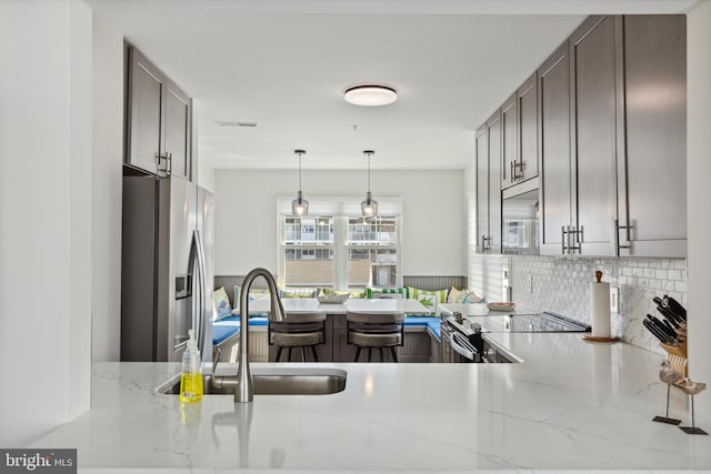 kitchen featuring a sink, tasteful backsplash, stainless steel appliances, light stone countertops, and hanging light fixtures