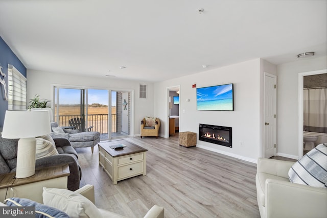 living area featuring visible vents, light wood-type flooring, baseboards, and a glass covered fireplace