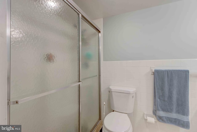 bathroom with a shower stall, toilet, tile walls, and wainscoting