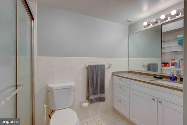 bathroom featuring vanity, a wainscoted wall, visible vents, tile walls, and toilet