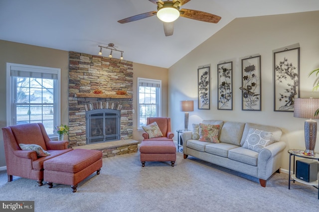 living area with a ceiling fan, baseboards, carpet floors, lofted ceiling, and a stone fireplace