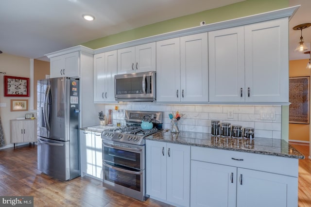 kitchen featuring decorative backsplash, stainless steel appliances, dark stone counters, and wood finished floors