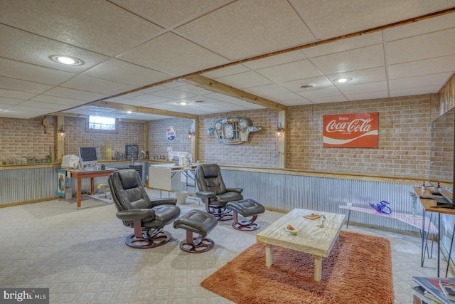 living area with a drop ceiling and brick wall