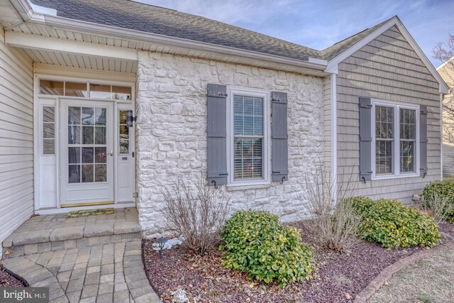 entrance to property with stone siding and a shingled roof