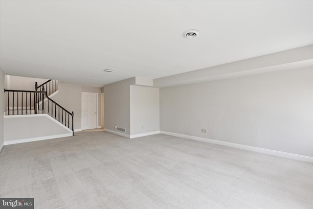 empty room featuring visible vents, light colored carpet, stairway, and baseboards