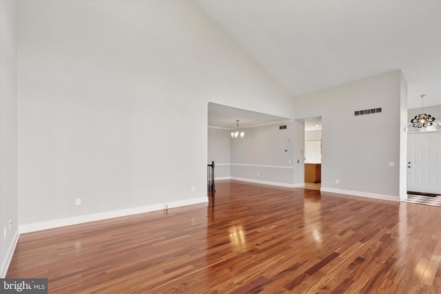 unfurnished living room featuring a notable chandelier, baseboards, visible vents, and wood finished floors