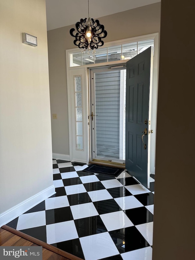 entryway with tile patterned floors, a chandelier, and baseboards