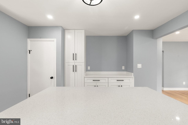 kitchen with light stone counters, wood finished floors, recessed lighting, white cabinets, and baseboards