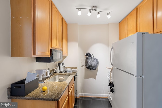 kitchen with dark tile patterned flooring, a sink, dark stone countertops, freestanding refrigerator, and baseboards