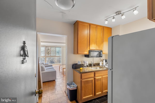 kitchen featuring black microwave, dark stone countertops, rail lighting, freestanding refrigerator, and a sink