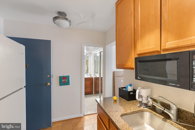 kitchen featuring light stone countertops, baseboards, black microwave, and a sink