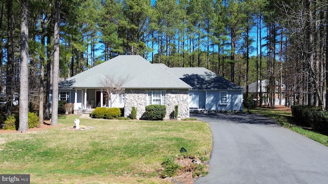 view of front of house featuring aphalt driveway, stone siding, and a front yard