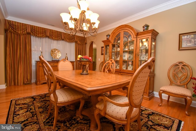 dining room featuring baseboards, a chandelier, ornamental molding, light wood-style floors, and arched walkways