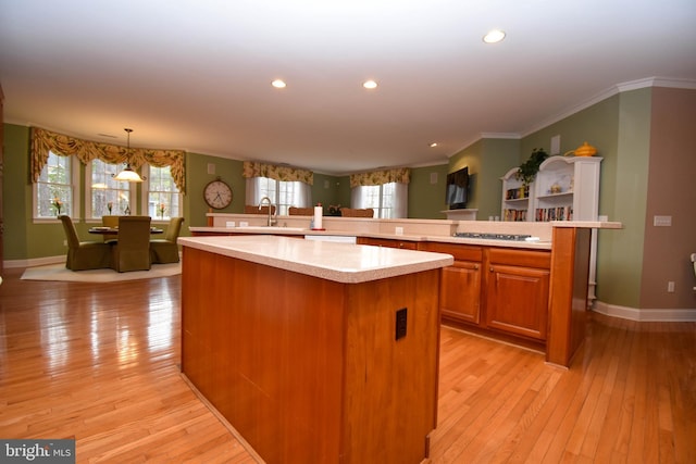 kitchen featuring a kitchen island, light countertops, ornamental molding, brown cabinets, and light wood-style floors