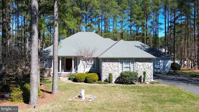 single story home with aphalt driveway, stone siding, a front lawn, and a shingled roof