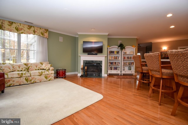 living area featuring visible vents, a premium fireplace, ornamental molding, recessed lighting, and wood finished floors