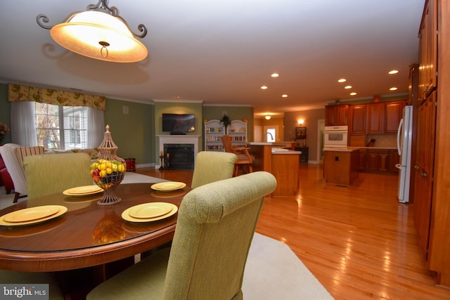 dining space with ornamental molding, a glass covered fireplace, recessed lighting, light wood finished floors, and baseboards