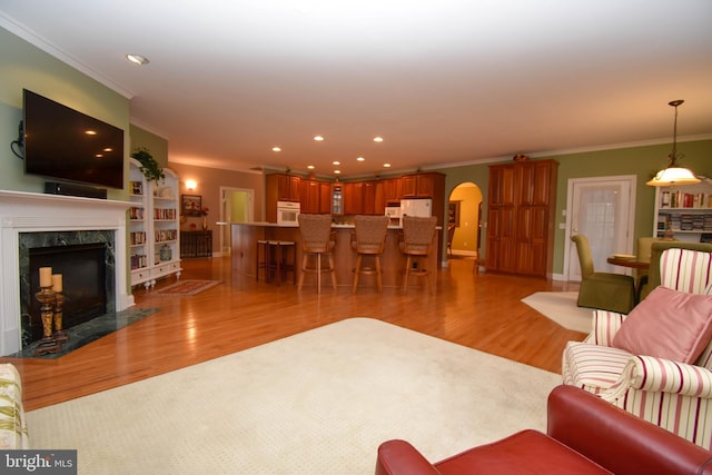 living area with recessed lighting, arched walkways, a high end fireplace, light wood-style floors, and crown molding