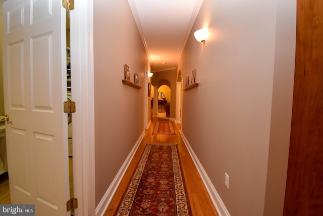 hall with crown molding, wood finished floors, arched walkways, and baseboards