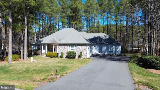 view of front facade featuring stone siding, a front lawn, driveway, and a shingled roof