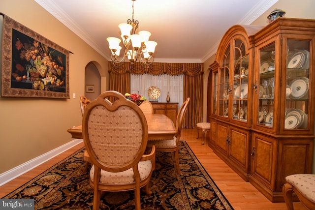 dining area featuring arched walkways, crown molding, light wood finished floors, baseboards, and a chandelier