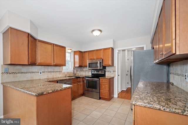 kitchen featuring brown cabinets, appliances with stainless steel finishes, a peninsula, stone counters, and light tile patterned floors