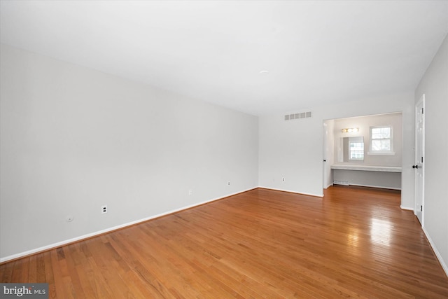 unfurnished room with visible vents, baseboards, and hardwood / wood-style flooring