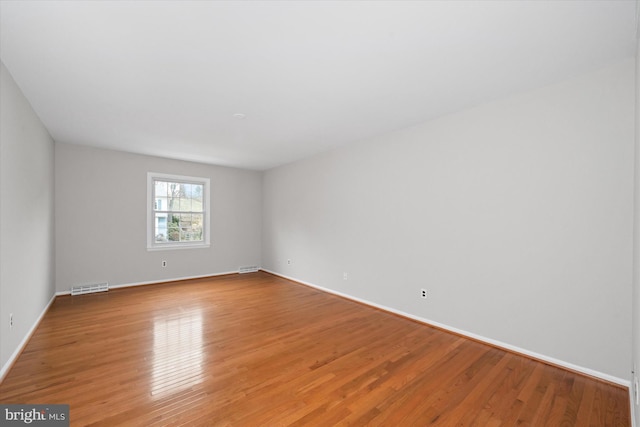 empty room featuring light wood-style floors, visible vents, and baseboards