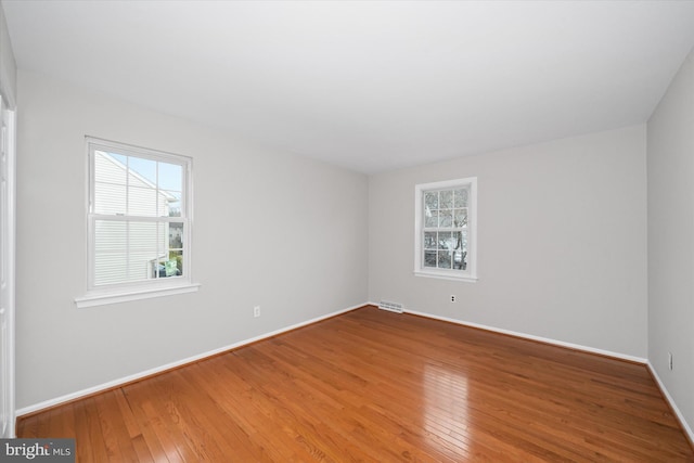 unfurnished room with hardwood / wood-style floors, baseboards, and visible vents