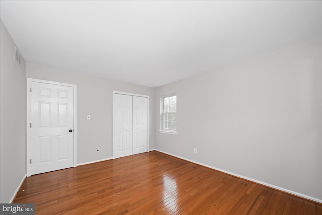 unfurnished bedroom with hardwood / wood-style floors, visible vents, baseboards, and a closet