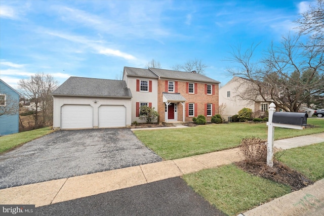 colonial inspired home with a front yard, an attached garage, a shingled roof, aphalt driveway, and brick siding