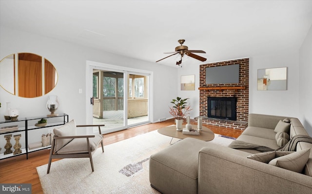 living area featuring a brick fireplace, a ceiling fan, and wood finished floors