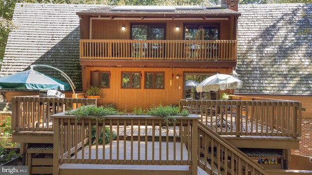 back of property featuring solar panels, a wooden deck, a balcony, and a chimney