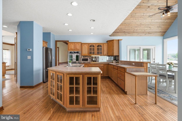 kitchen with a peninsula, an island with sink, glass insert cabinets, appliances with stainless steel finishes, and light wood-type flooring