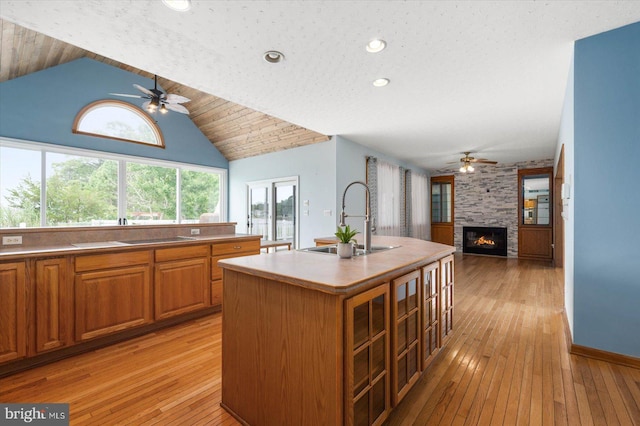 kitchen featuring a sink, a large fireplace, brown cabinetry, and ceiling fan