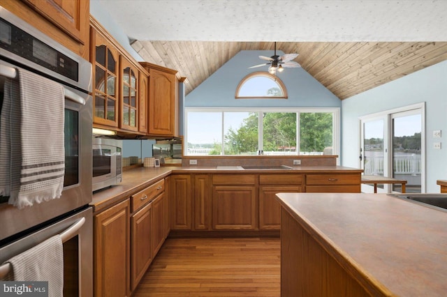 kitchen featuring ceiling fan, brown cabinetry, glass insert cabinets, and stainless steel double oven