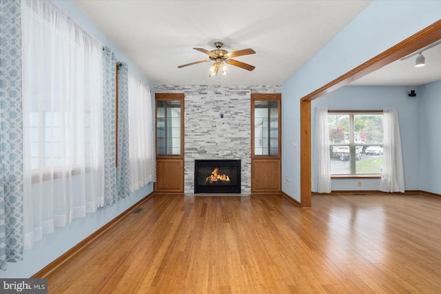 unfurnished living room with a stone fireplace, baseboards, ceiling fan, and wood finished floors