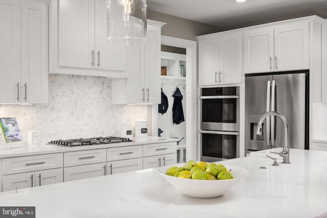 kitchen featuring pendant lighting, appliances with stainless steel finishes, white cabinets, decorative backsplash, and light stone countertops