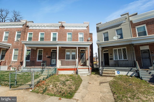 view of property featuring brick siding, a porch, and fence