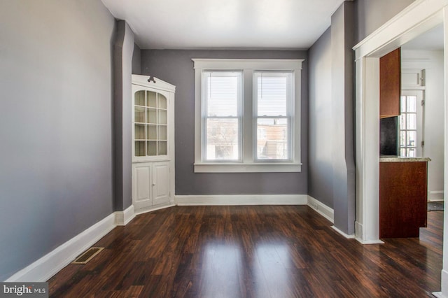 unfurnished room featuring dark wood finished floors, visible vents, and baseboards