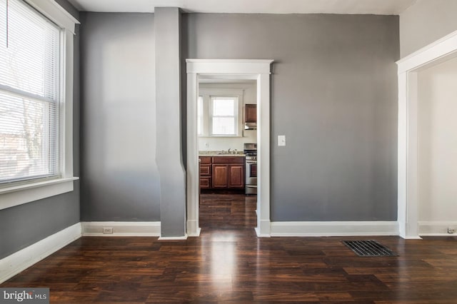 empty room featuring a wealth of natural light, visible vents, and dark wood-style floors