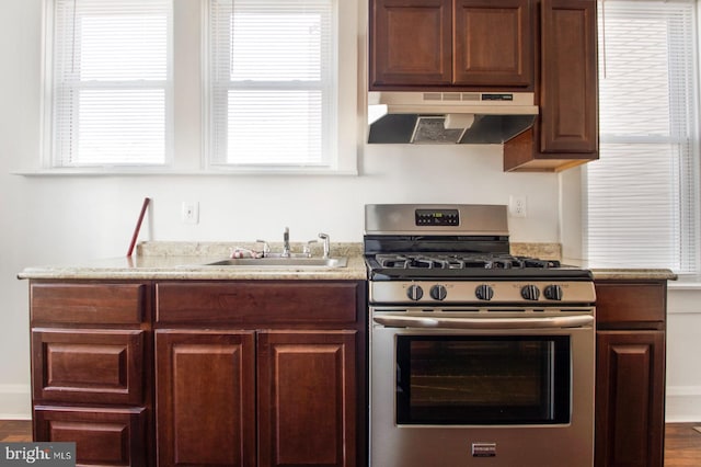 kitchen with under cabinet range hood, gas range, a healthy amount of sunlight, and a sink