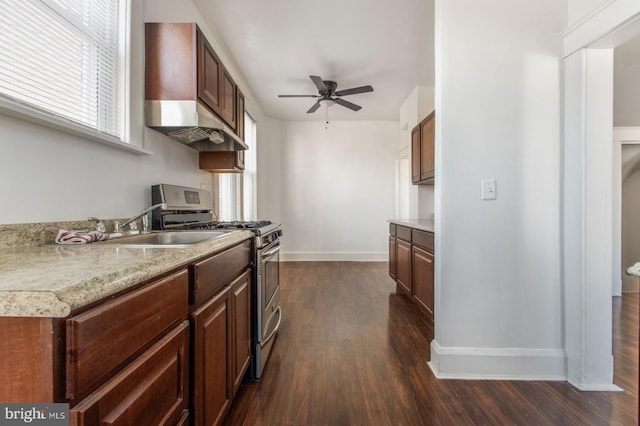 kitchen featuring dark wood finished floors, ceiling fan, light countertops, wall chimney exhaust hood, and stainless steel gas stove