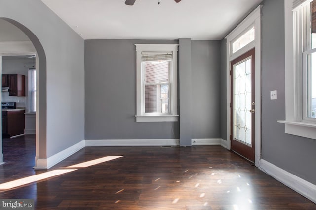 entryway featuring wood finished floors, a ceiling fan, arched walkways, and baseboards