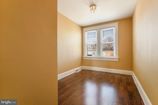 empty room with dark wood-style floors, visible vents, and baseboards