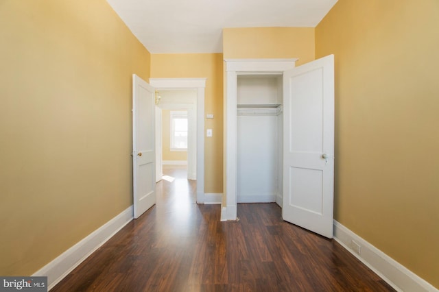 unfurnished bedroom featuring dark wood finished floors, baseboards, and a closet