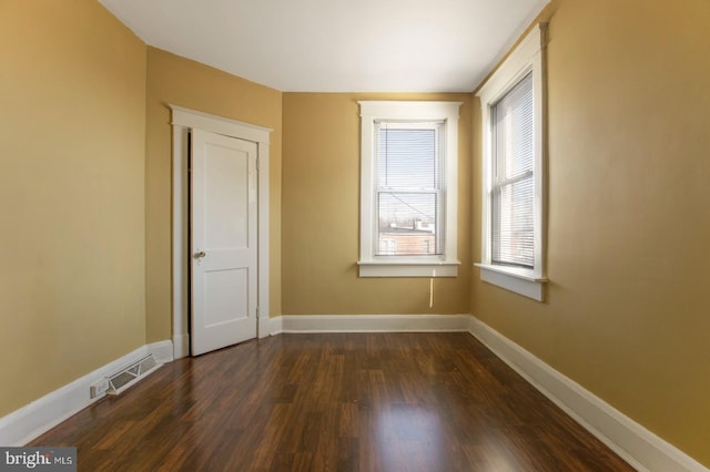 empty room with visible vents, dark wood-type flooring, and baseboards